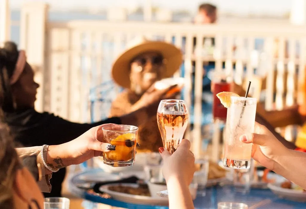 Close-up of four hands toasting diverse drinks outdoors.