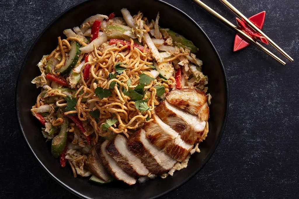 Asian chicken and vegetable bowl with noodles, cilantro, and gold chopsticks.