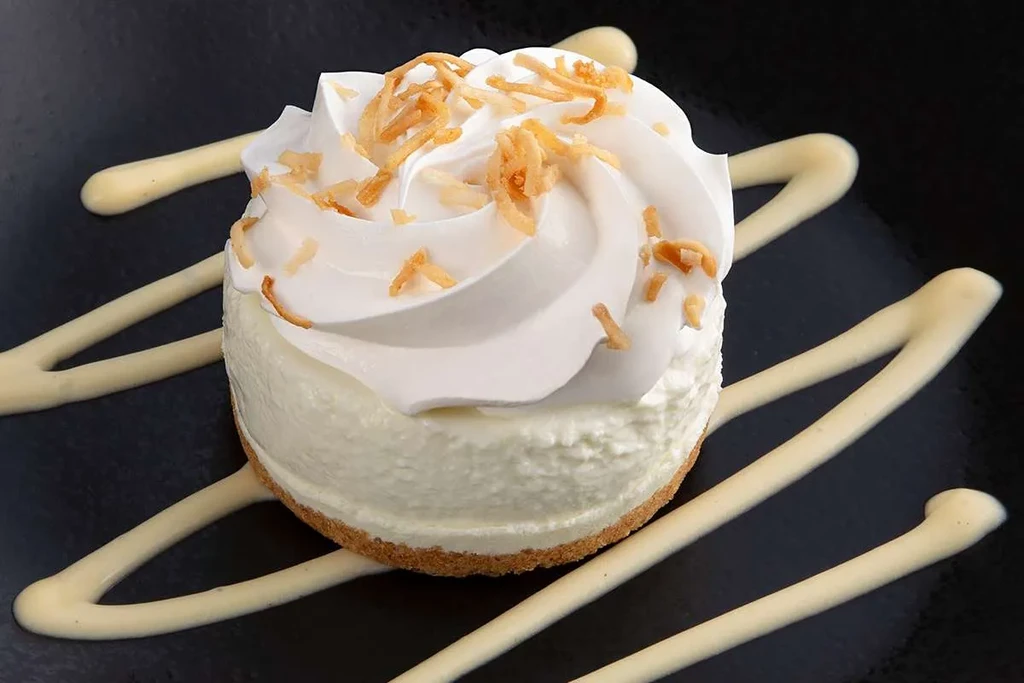 Creamy dessert with graham crust, whipped cream, coconut, and sauce drizzles.