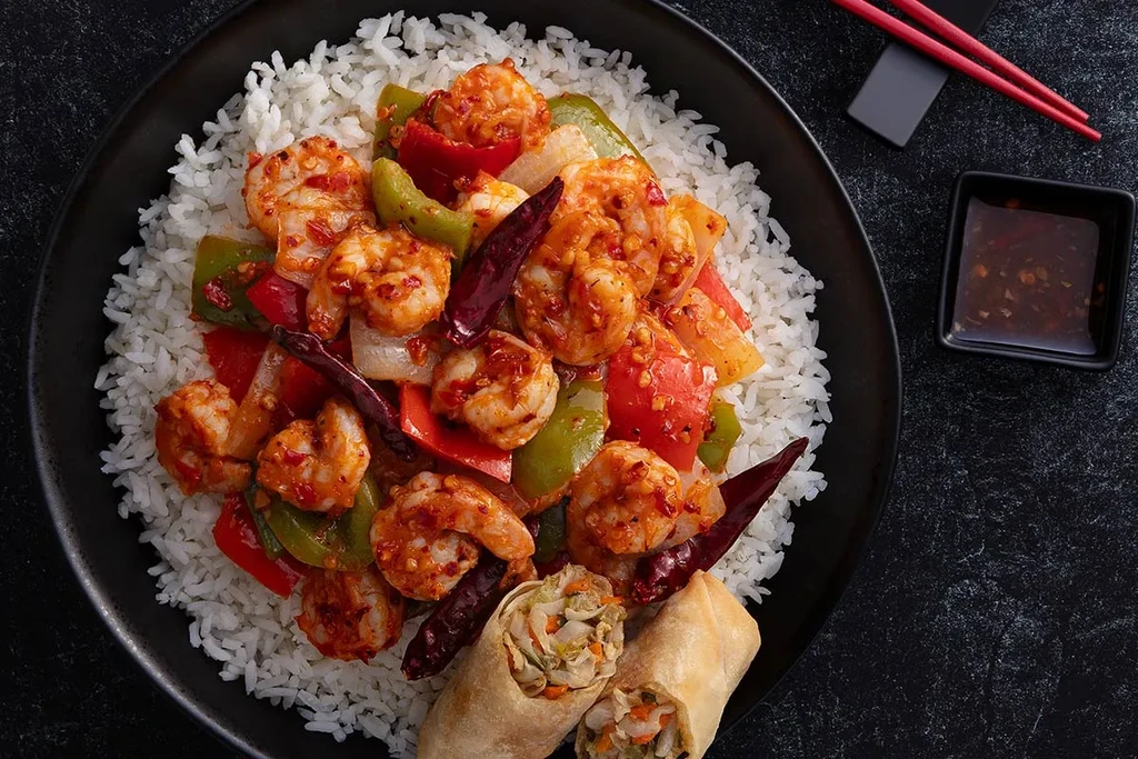 Overhead: spicy Chinese-American shrimp, rice, egg rolls, chopsticks, dipping sauce.