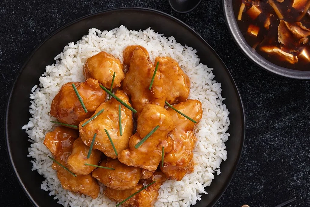 Orange chicken and rice with chives, next to a dark soup.