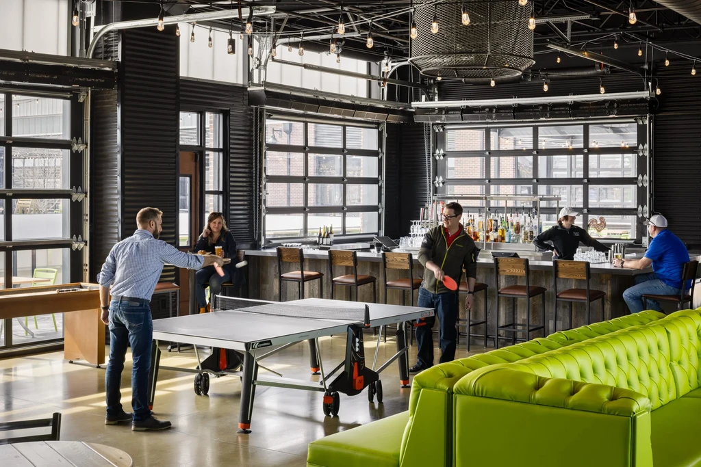People play ping-pong in a modern industrial bar with shuffleboard.