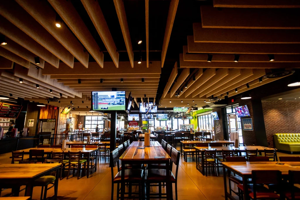Modern sports bar with slatted ceiling, wooden tables, and large TVs.