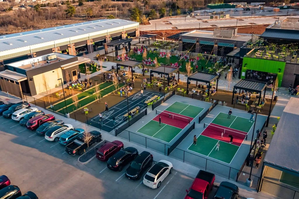 Dusk aerial photo of an outdoor complex with pickleball, dining, and people.