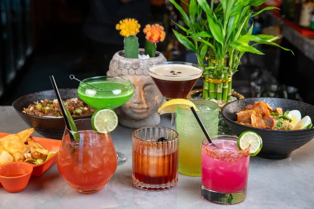 Colorful cocktails, crispy pork belly, and wontons on a textured bar table.