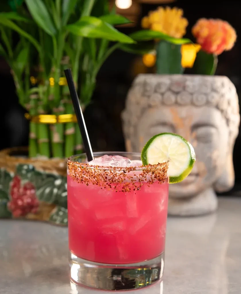 Pink cocktail in a short glass with lime, straw, and spiced rim.
