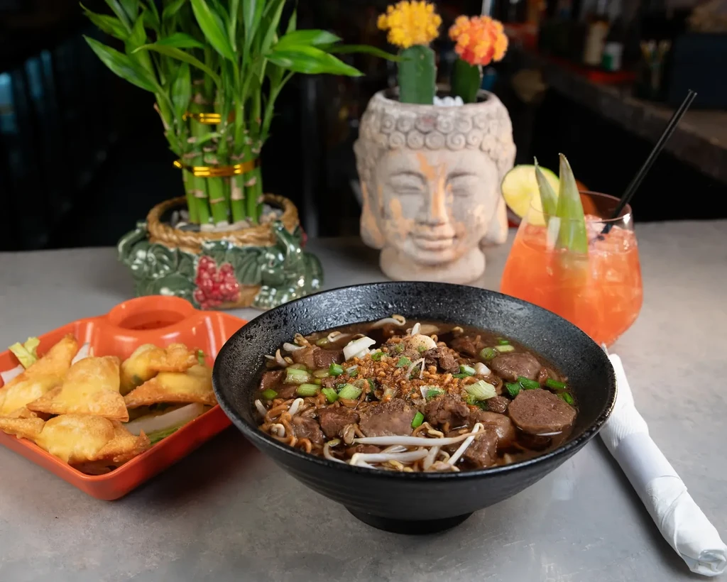 A meal of noodle soup, fried wontons, and a garnished cocktail.
