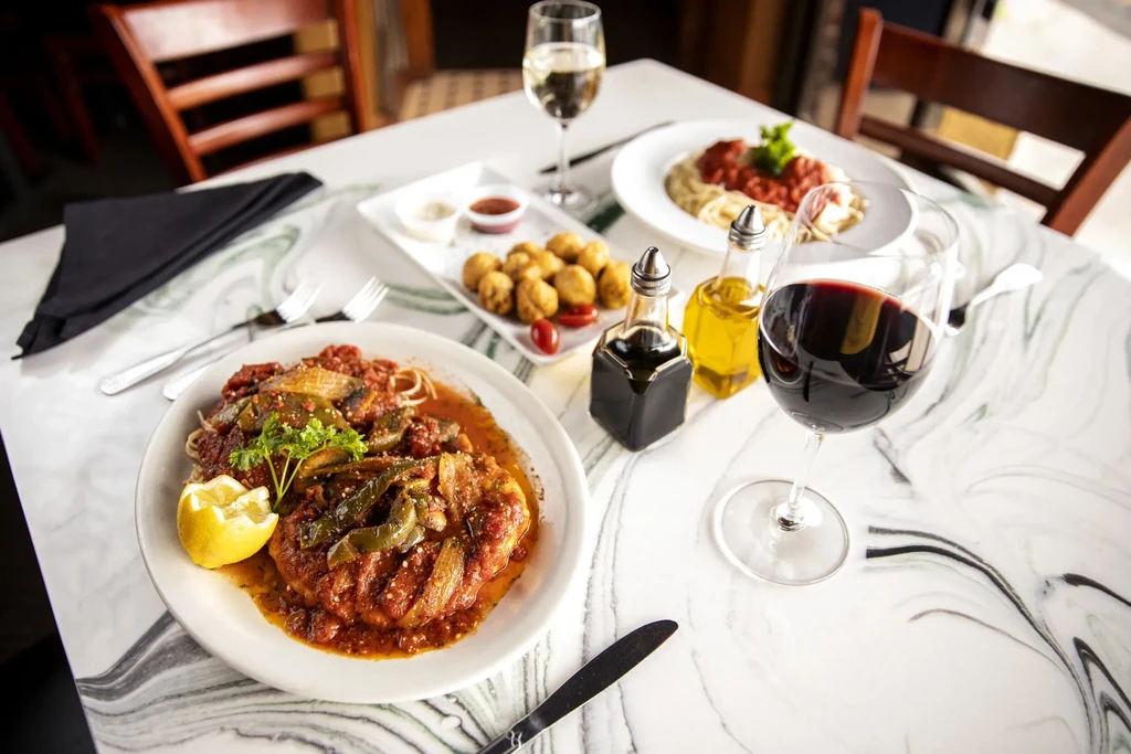 Restaurant table with a hearty meal, pasta, fried appetizers, and wine.
