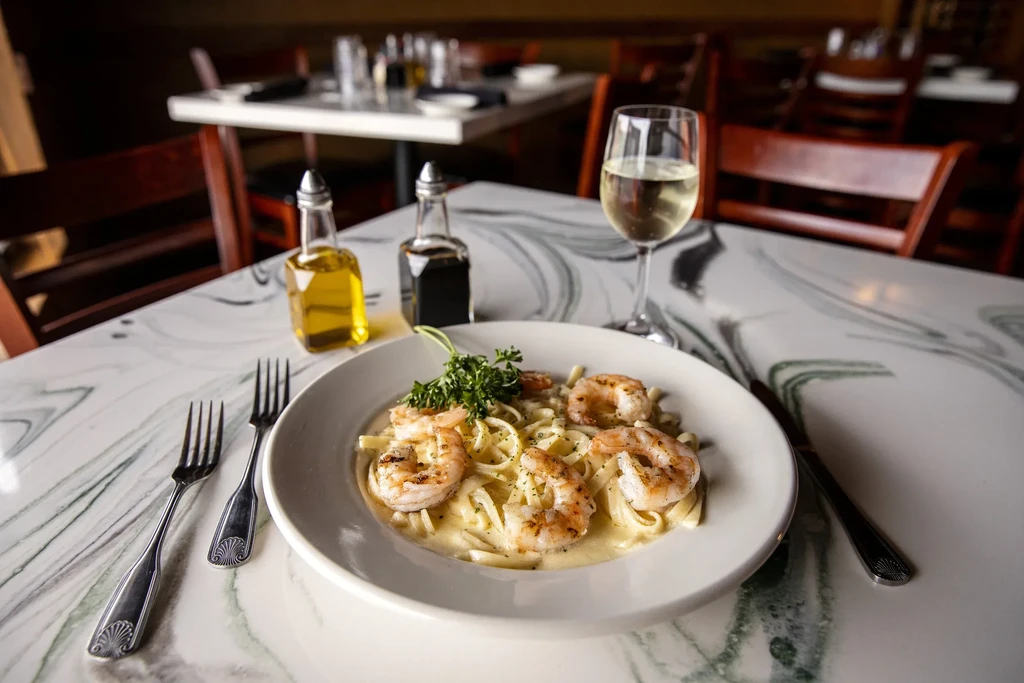Creamy shrimp fettuccine in a white bowl with wine, olive oil.