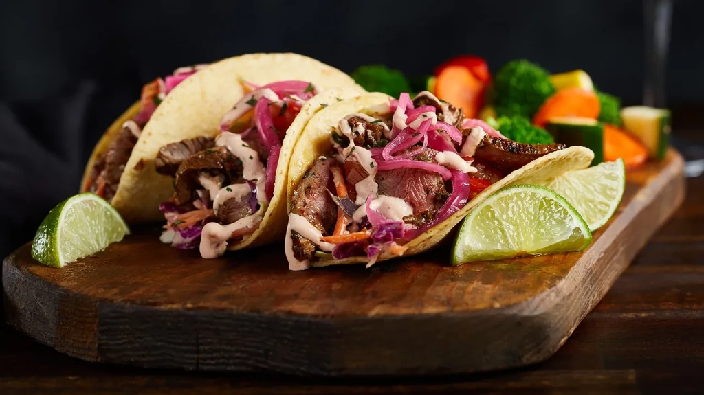 Three beef tacos with cabbage, pickled onions, and lime on wood.