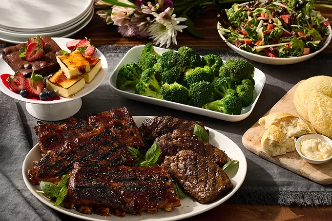 A table spread with BBQ ribs, steak, salad, broccoli, and desserts.