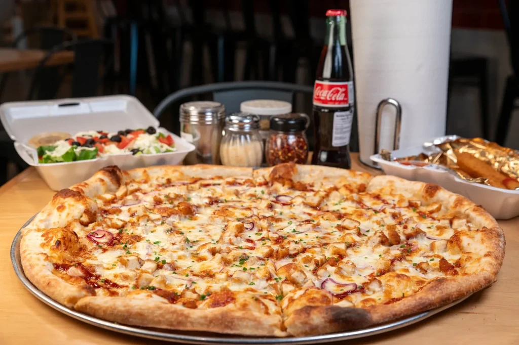 Chicken BBQ pizza, salad, and sides on a restaurant table.