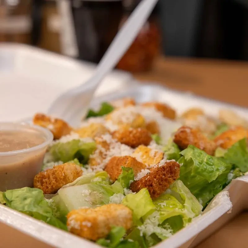 Rectangular takeout container holds salad, lettuce, croutons, cheese, dressing.