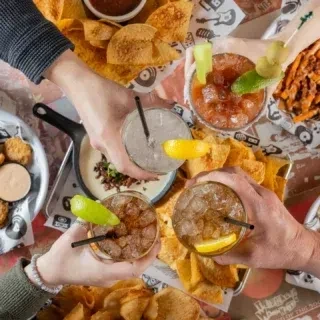 Overhead view: four hands holding cocktails among appetizers.