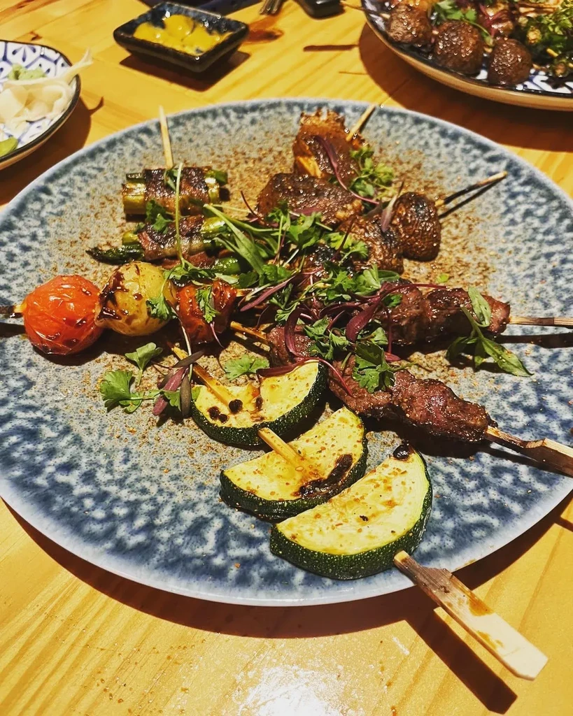 Various grilled meat and vegetable skewers on a patterned plate.