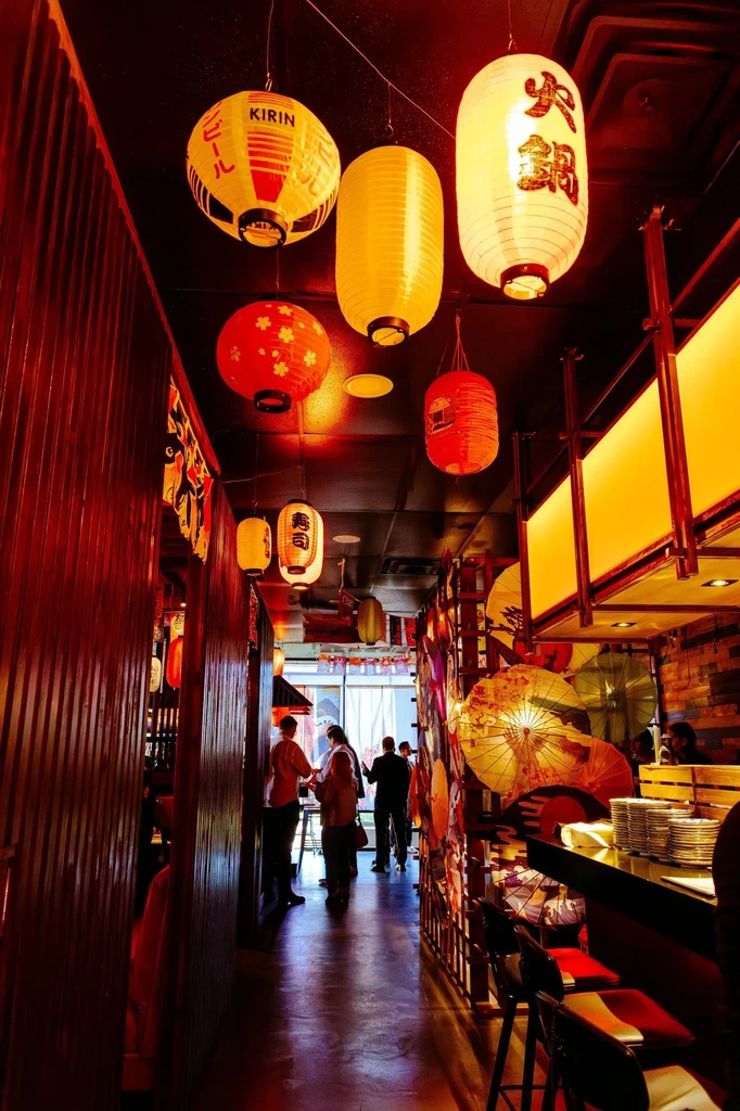 Japanese restaurant hallway with many paper lanterns, wooden walls, and guests.