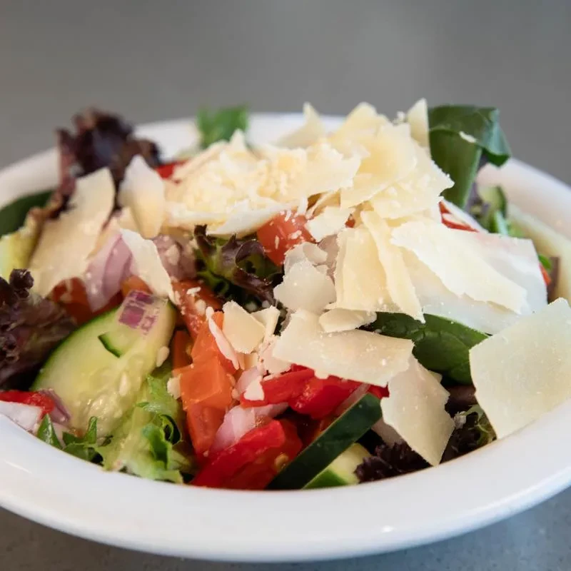 Fresh salad with mixed greens, tomato, cucumber, Parmesan in white bowl.