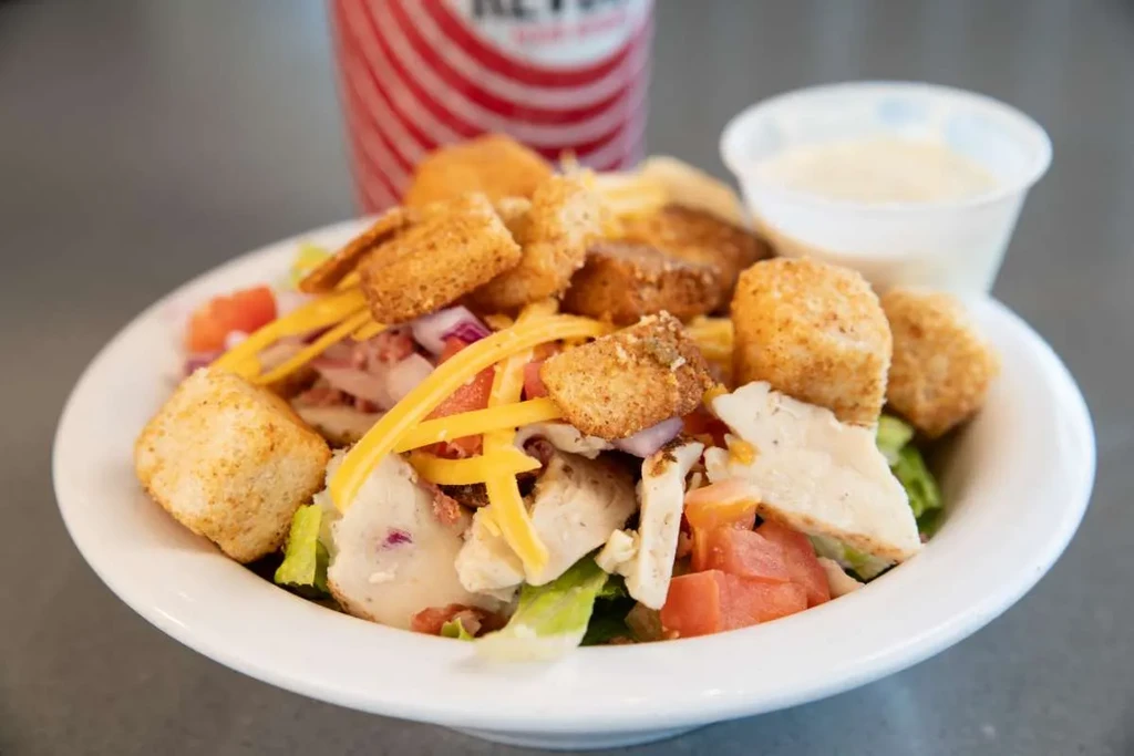 Colorful chicken salad with lettuce, tomato, cheese, croutons, and dressing.