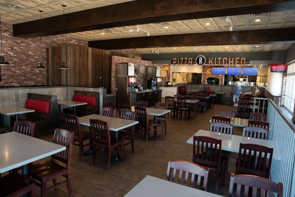 Restaurant interior featuring red booths, exposed brick, and a "PIZZA R KITCHEN" sign.