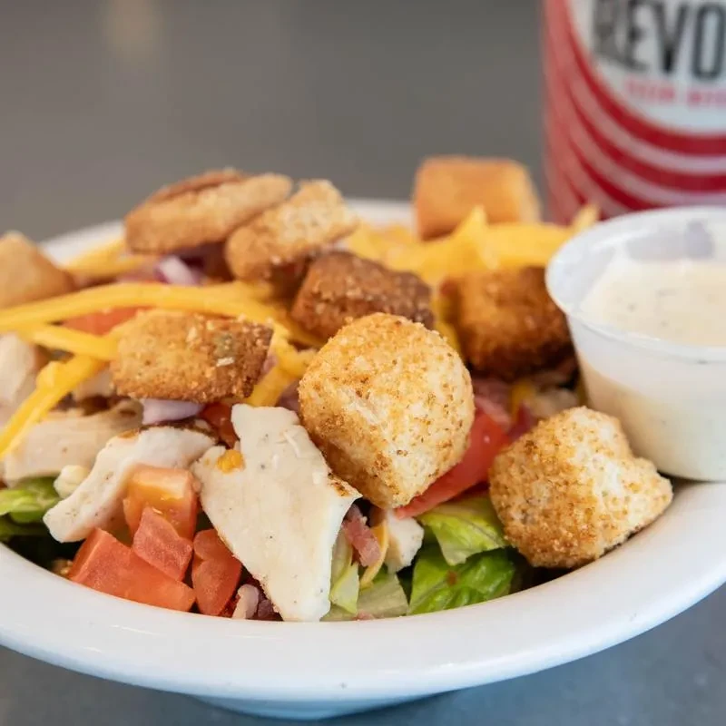 Close-up of chicken salad with lettuce, tomatoes, cheese, croutons, and ranch.