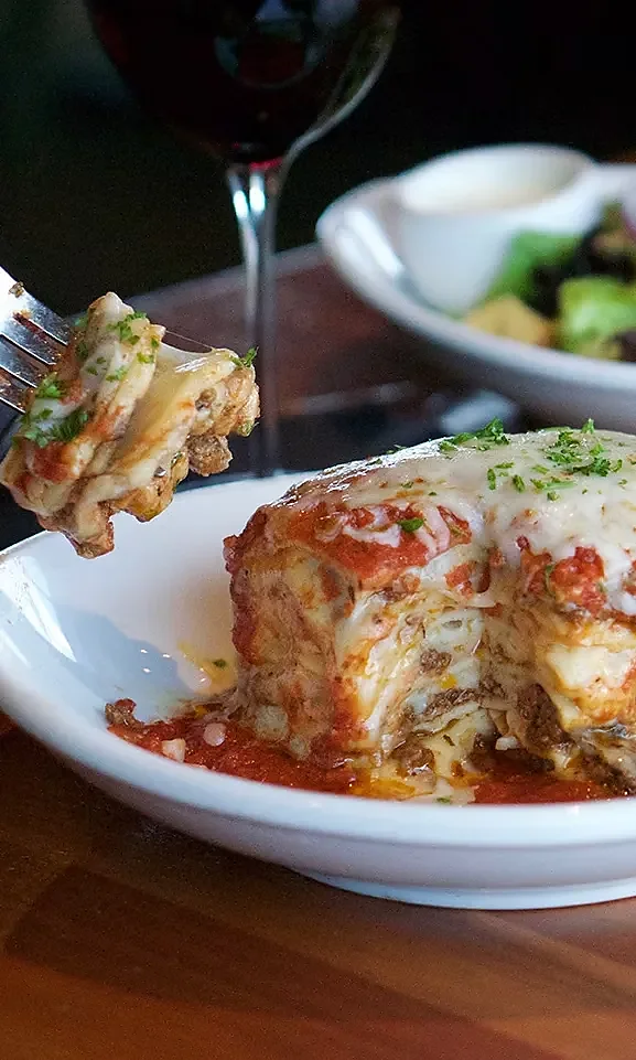 Layered beef lasagna with melted cheese and marinara, forkful lifted above plate