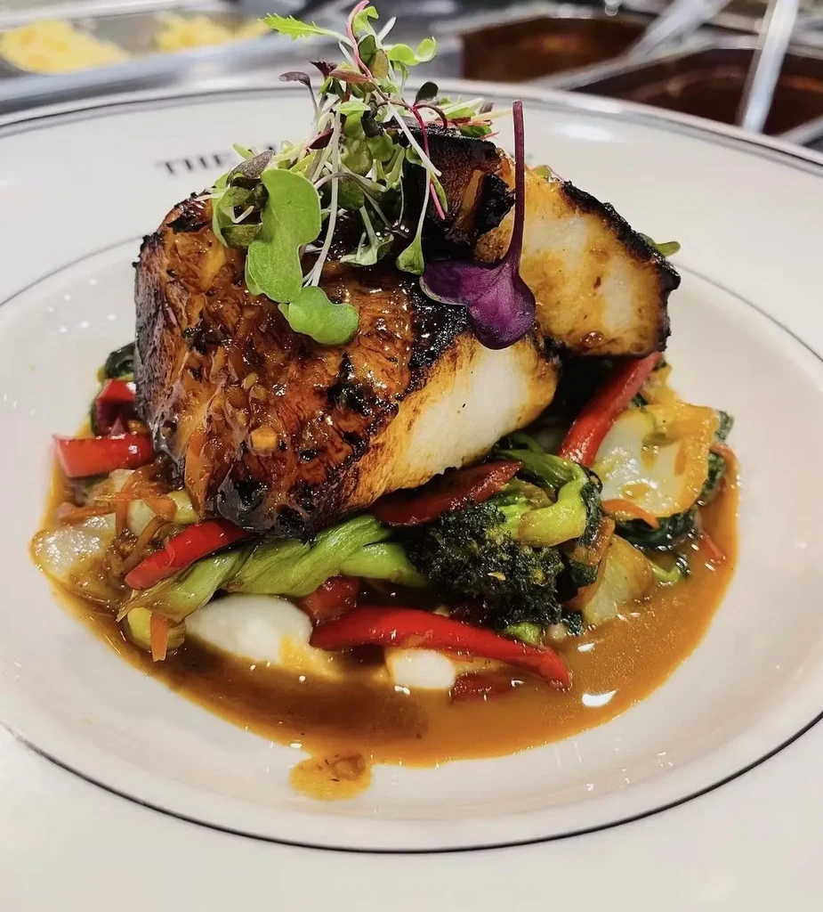 A piece of glazed fish on a bed of vegetables with sauce.