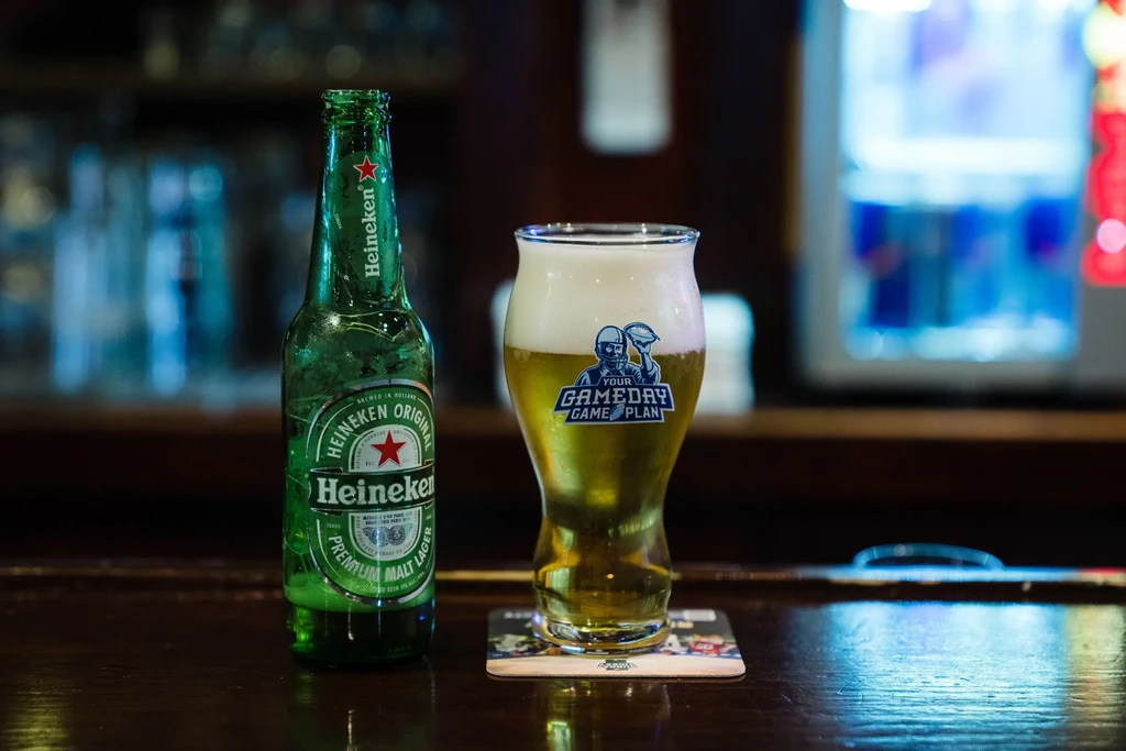 A Heineken bottle and a glass of beer on a bar counter.