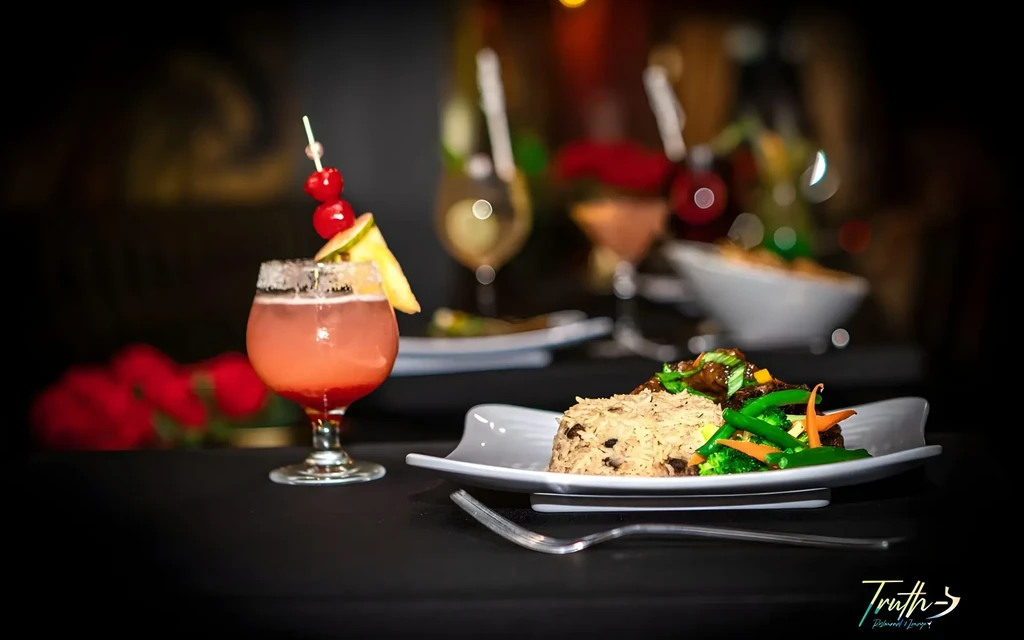 Plate of rice and vegetables with a pink cocktail, dark background.