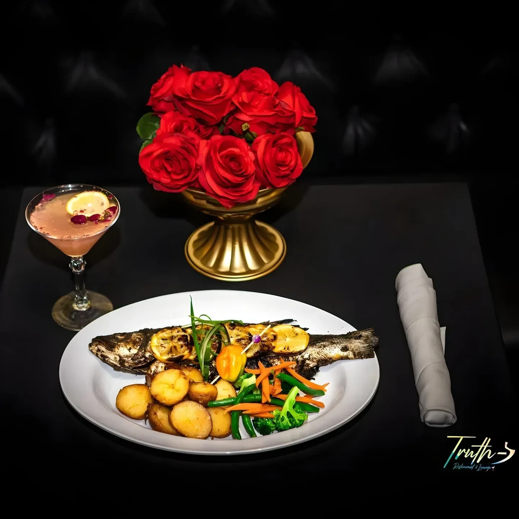 A martini, a whole grilled fish, and a vase of red roses.