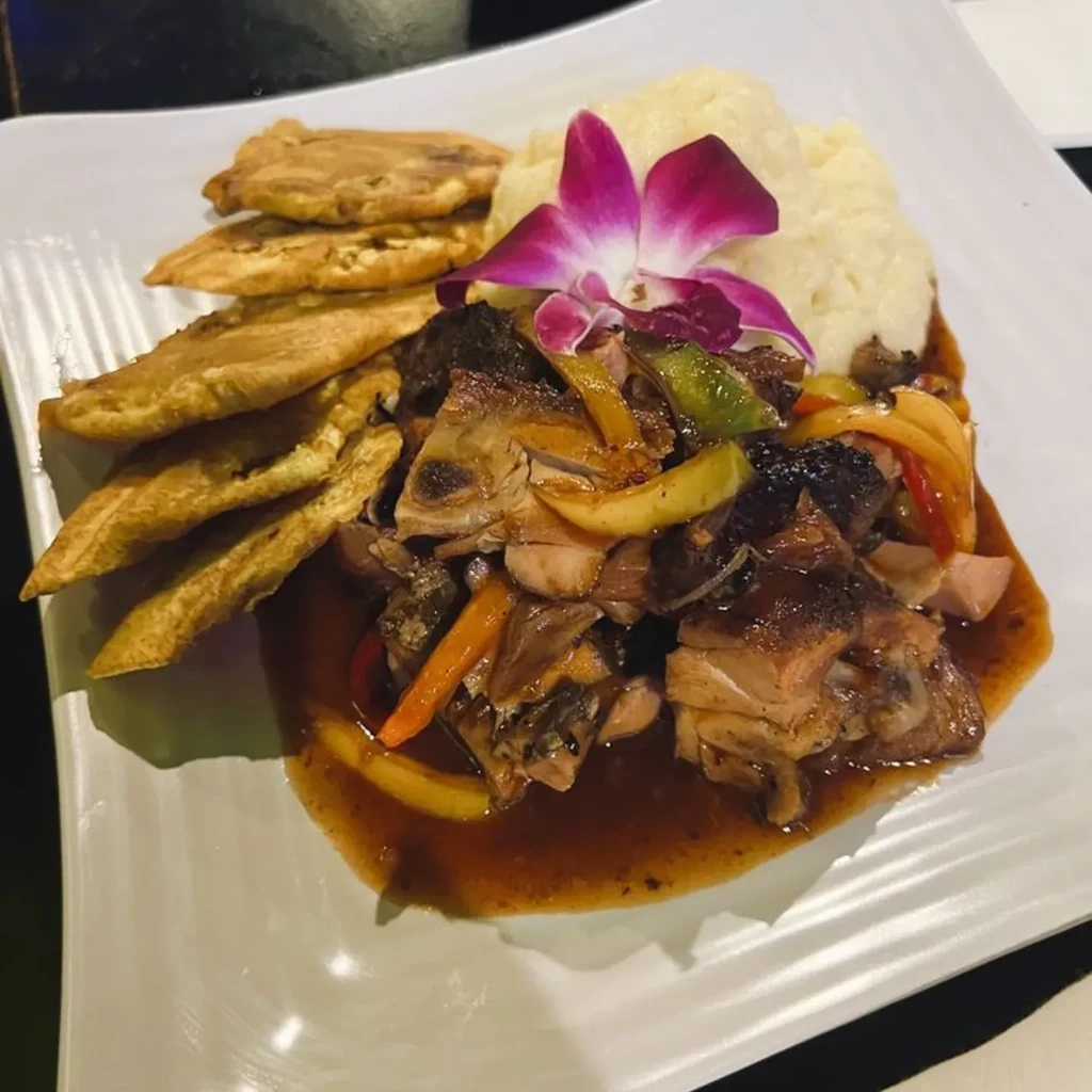 Mashed potatoes, meat, vegetables, and plantains, garnished with a purple orchid.