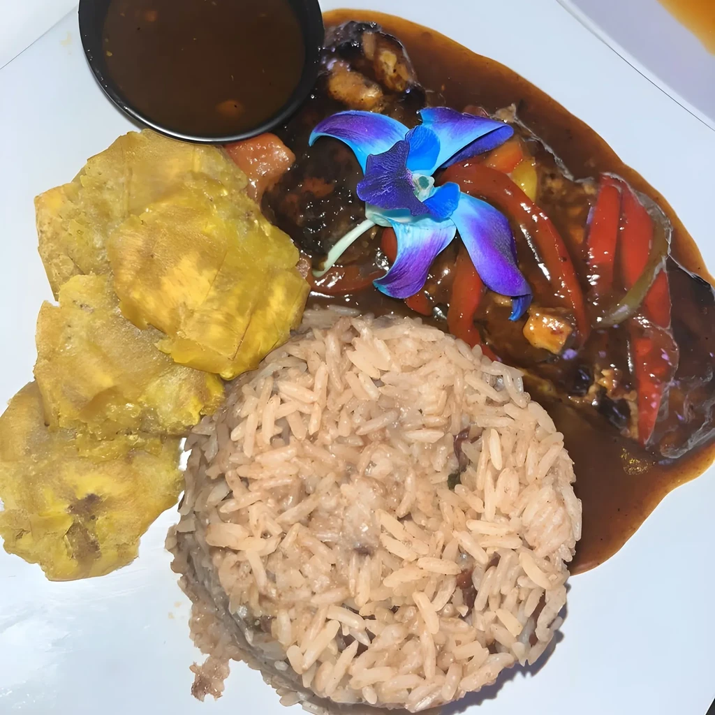 Stewed chicken, rice, plantains, and sauce, garnished with an orchid.