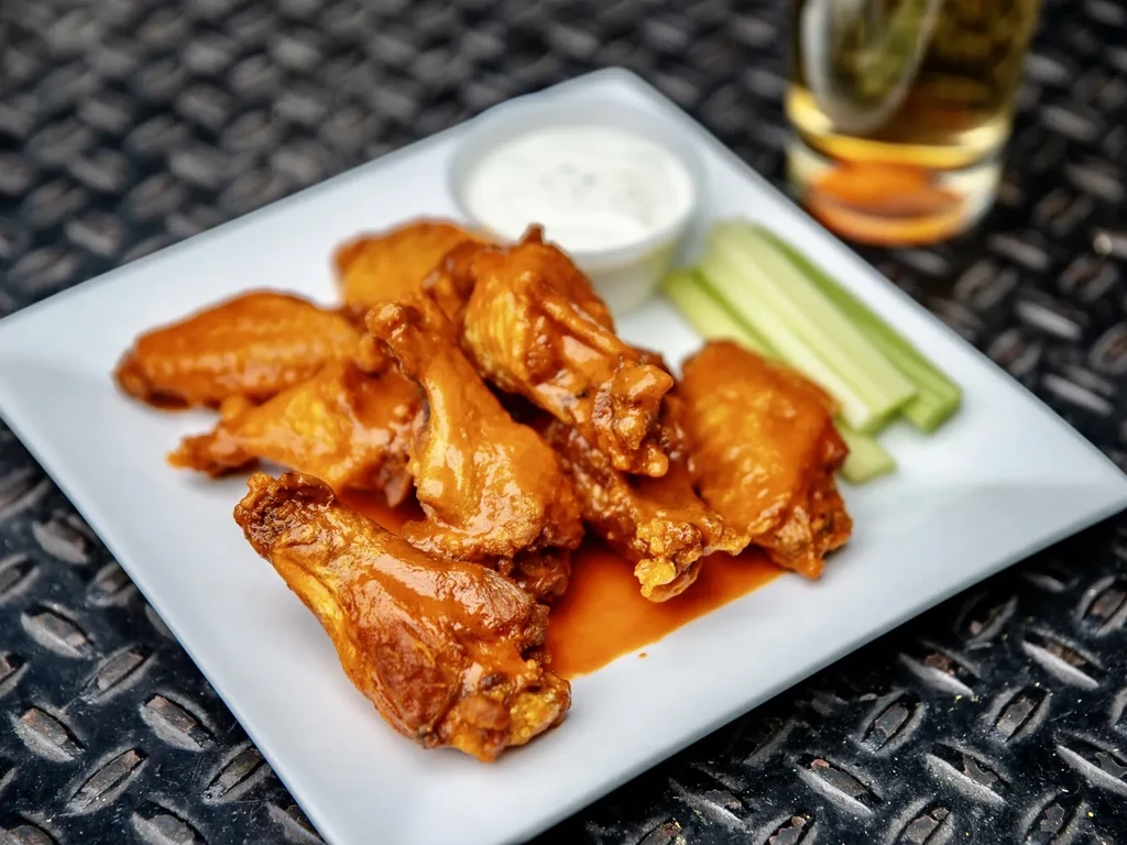 Saucy chicken wings, celery sticks, and dip on a white plate.