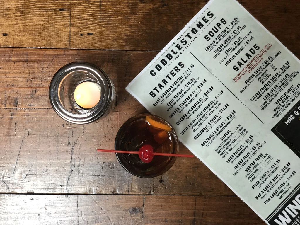 Overhead view of a lit candle, drink, and menu on wood table.