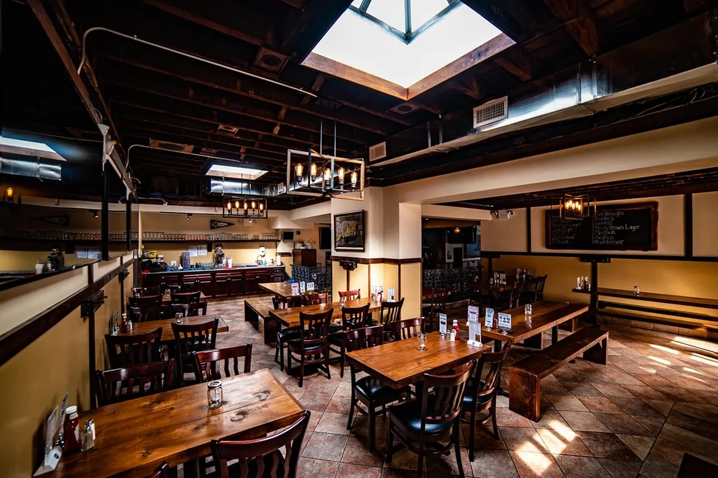 Restaurant interior with wooden tables, exposed beams, skylights, and bar area.