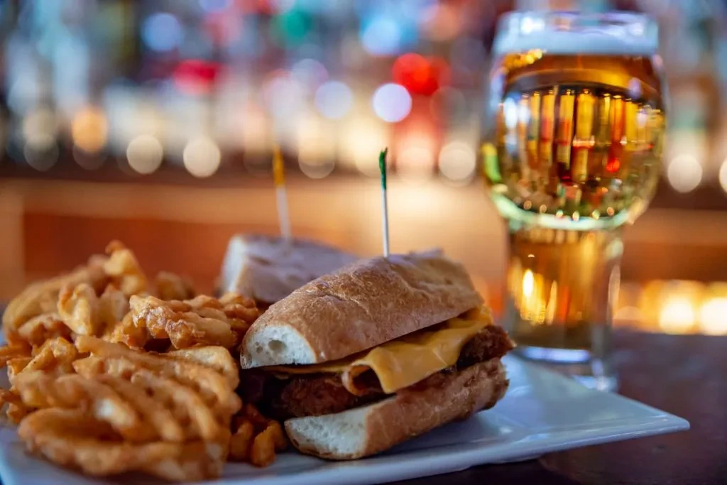 A beer, sandwich, and waffle fries on a bar counter.