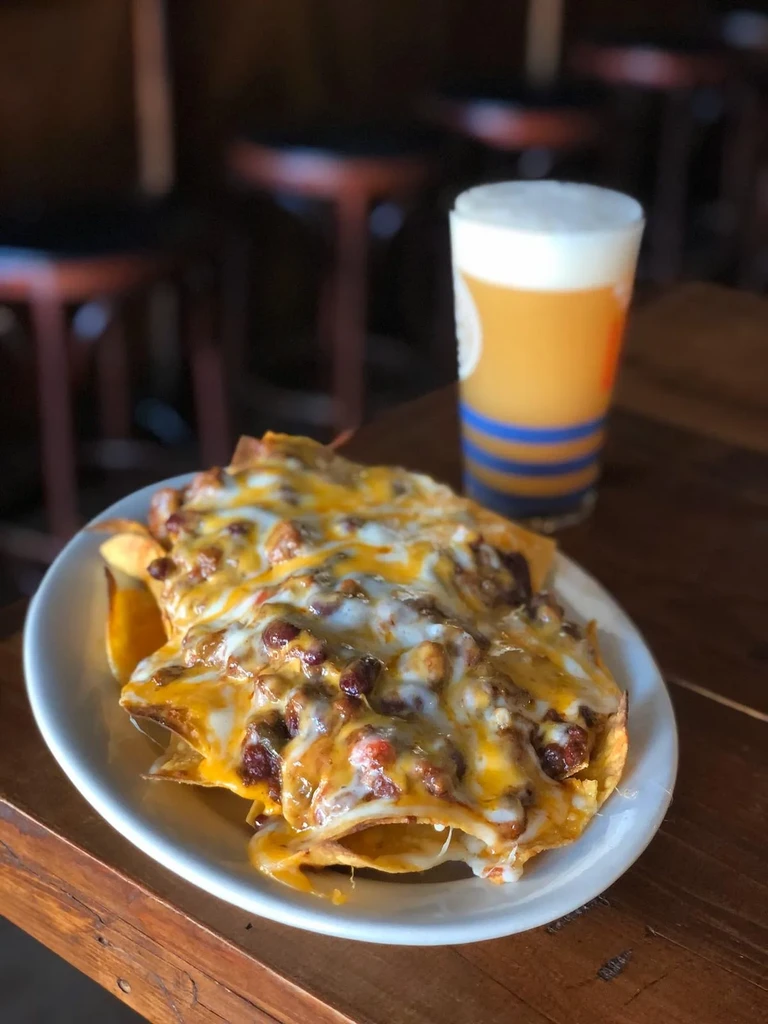 Plate of nachos with melted cheese and chili next to a glass of beer.