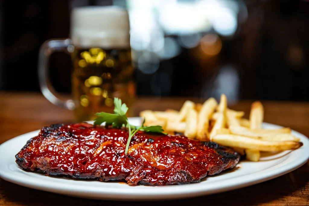Red-glazed meat, fries, and a beer on a plate.