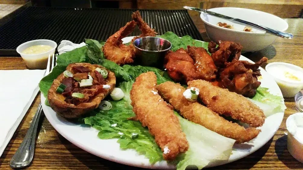 A platter of fried seafood, chicken wings, and potato skins on lettuce.