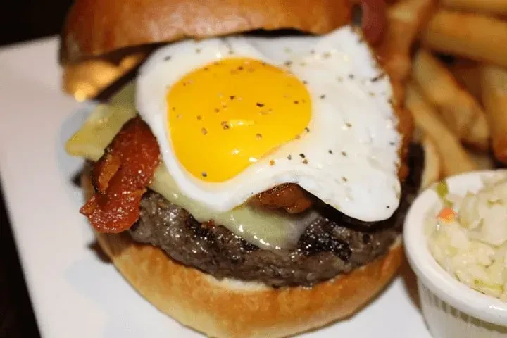 Close-up of a burger with a fried egg, bacon, and fries.