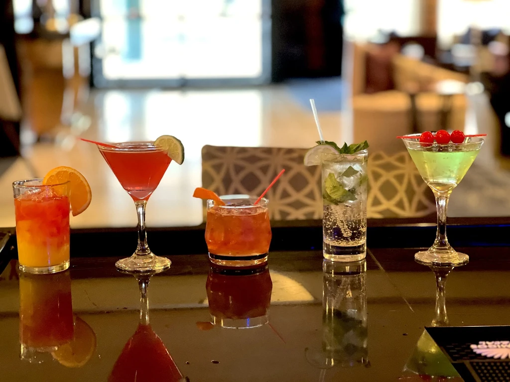 Five colorful cocktails sit on a glossy black bar.