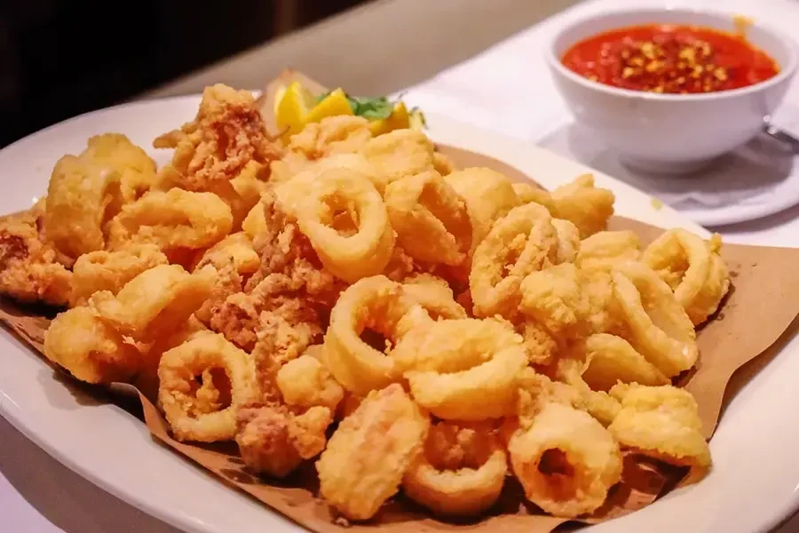 A white plate filled with fried calamari and a side of marinara sauce.