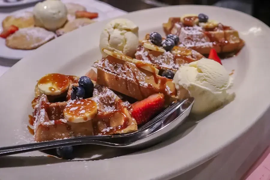 Waffles with fruit, caramel, powdered sugar, and scoops of ice cream.