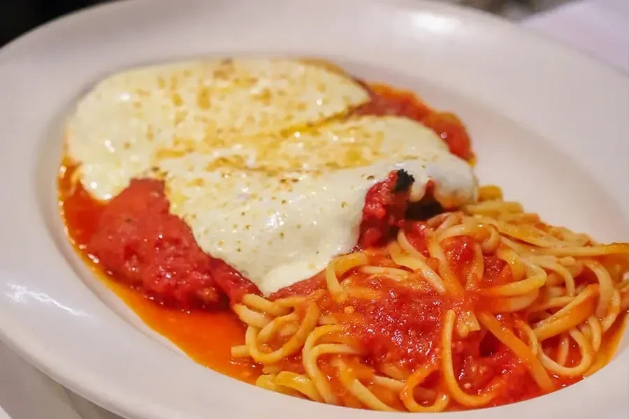 Chicken parmesan covered in red sauce and cheese, with linguini.