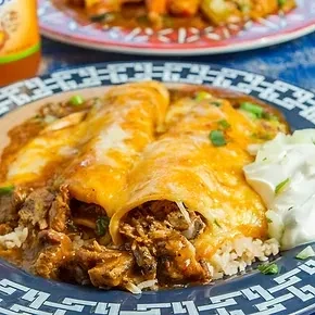 Two enchiladas topped with cheese, rice, and sour cream on a blue plate.