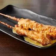 Two chicken skewers coated in cheese sauce on a dark plate.