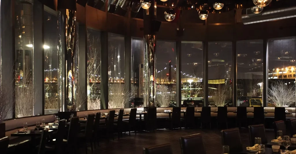 Dark, empty restaurant with a city skyline view at night.