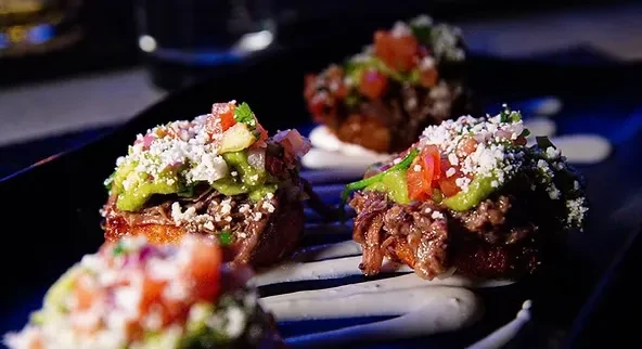 Four shredded beef appetizers with guacamole, salsa, and cheese.