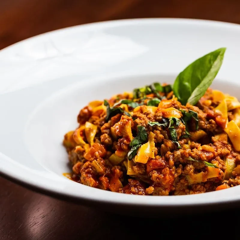 Pasta bolognese with fresh basil in a white bowl.