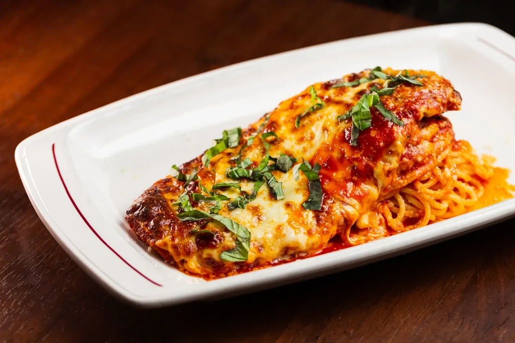 Chicken parmesan with pasta on a white rectangular plate.