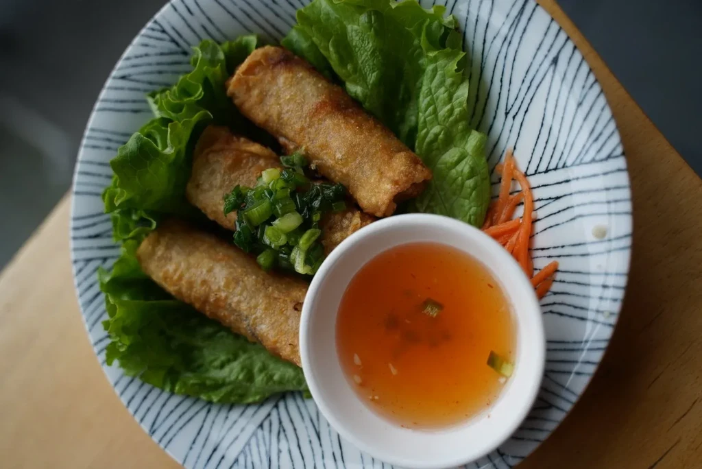 Three fried spring rolls, lettuce, chopped scallions, and dipping sauce.